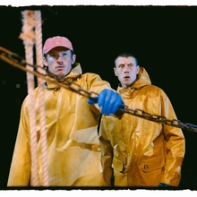 Two people wearing yellow raincoats and one with blue gloves handling a chain on a boat at night.