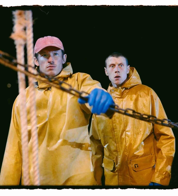 Two people wearing yellow raincoats and one with blue gloves handling a chain on a boat at night.