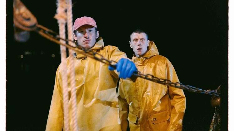 Two people wearing yellow raincoats and one with blue gloves handling a chain on a boat at night.