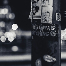 A black and white image of a lamp post with text written on it - the text reads "Big Data is Watching You", and is written on the lamp post with white ink on the black structure. 