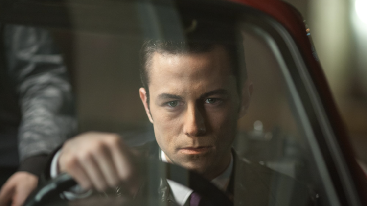 Person holding steering wheel inside a car at night, viewed through the windshield with a passenger's arm visible.