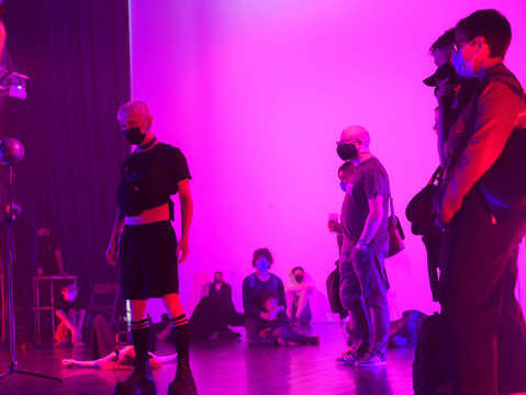 People in black clothes, wearing masks and breathing.systems equipment on their chests. The lighting is dimmed, purple and pink. 