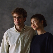 A man in a white shirt and a woman in a black jumper stand next to each other and smile looking away from the camera.