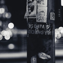 A black and white image of a lamp post with text written on it - the text reads "Big Data is Watching You", and is written on the lamp post with white ink on the black structure. 