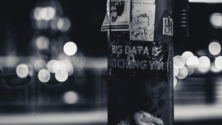 A black and white image of a lamp post with text written on it - the text reads "Big Data is Watching You", and is written on the lamp post with white ink on the black structure. 