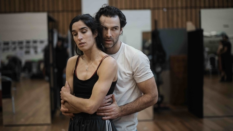 Two people rehearsing in a studio with wooden floors and mirrors.