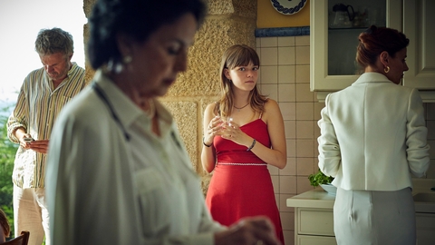 A still from Romeria of a girl in a red dress standing in a kitchen