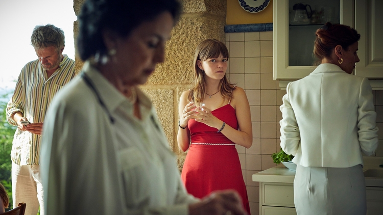 A still from Romeria of a girl in a red dress standing in a kitchen