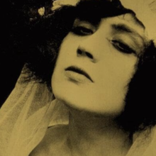 Sepia-toned close-up of a person wearing a textured garment, with dark background and partially visible hair and shoulder.