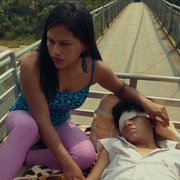 Two people sitting on a truck bed, one sitting upright and comforting the other lying down on a blanket.