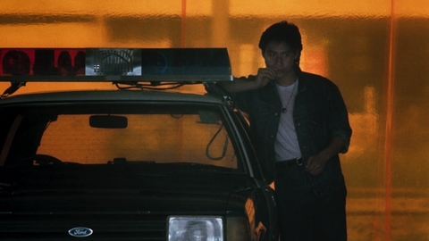A still from As Tears Go By of a person leaning against a police car, set against a glowing orange background.