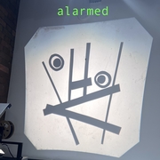 A projection on a wall shows abstract shapes resembling a surprised face. Above it, the word "alarmed" is written in green. The tone is humorous.