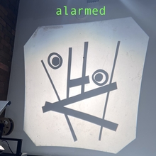 A projection on a wall shows abstract shapes resembling a surprised face. Above it, the word "alarmed" is written in green. The tone is humorous.