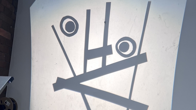 A projection on a wall shows abstract shapes resembling a surprised face. Above it, the word "alarmed" is written in green. The tone is humorous.