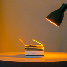 An image of Sister Sylvester's hand made book Constantinopoliad lying flat on a table, illuminated in a warm orange by a nearby desk lamp. 