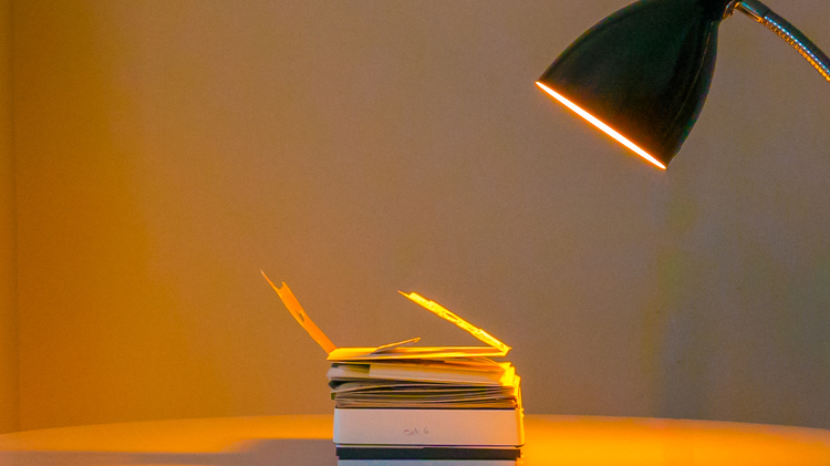 An image of Sister Sylvester's hand made book Constantinopoliad lying flat on a table, illuminated in a warm orange by a nearby desk lamp. 