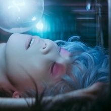 A still from 2046 of a person with blue hair and pink eyeshadow looks up at a floating bubble in dim, colorful lighting.