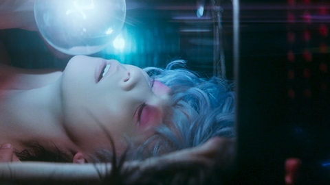A still from 2046 of a person with blue hair and pink eyeshadow looks up at a floating bubble in dim, colorful lighting.