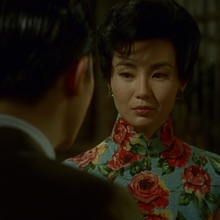 In still from In the Mood for Love of a man in a dark suit facing a woman wearing a blue floral qipao on a dimly lit street at night.