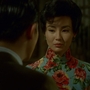 In still from In the Mood for Love of a man in a dark suit facing a woman wearing a blue floral qipao on a dimly lit street at night.