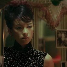 A still from 2046 of a person in a sleeveless, sparkly black top standing in front of a mirror decorated with various black-and-white photos.