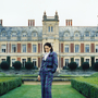 A still from Lady of a person standing outside a country manor is a tartan suit.