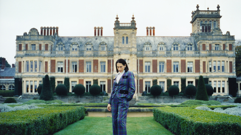 A still from Lady of a person standing outside a country manor is a tartan suit.