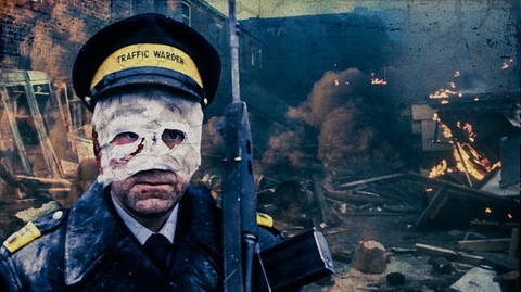 A traffic warden in uniform and cap stands amid a war-torn street with smoke, debris, and flames in the background.