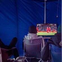 An image of men watching TV in a refugee camp. 
