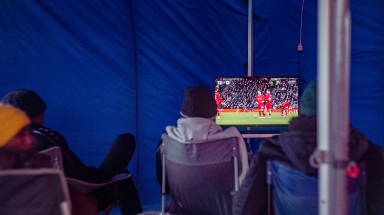 An image of men watching TV in a refugee camp. 