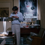 A still from Closed Circuit of two men in a cluttered office, one sitting and one standing, surrounded by film reels, a vintage lamp, and posters on the wall.