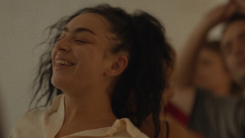 A still from Erupcja of a woman in a cream shirt in with dark hair in foreground, two others blurred in background.