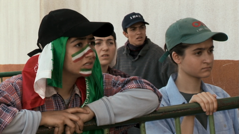 A group of four people leaning on a green metal railing, wearing casual clothes and baseball caps.