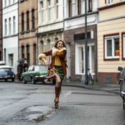 Person joyfully splashing through a puddle on a street lined with parked vintage cars and old buildings.