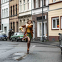 Person joyfully splashing through a puddle on a street lined with parked vintage cars and old buildings.