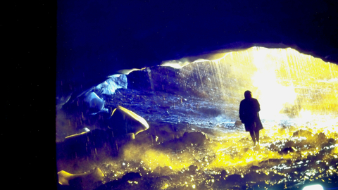 An over-exposed photo of a silhouette of a man walking through an icy cave.