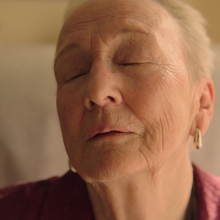 A woman with her eyes closed sitting up in bed.