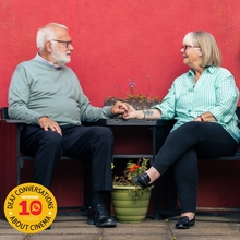 A couple sit at a table holding hands and smiling lovingly at one another