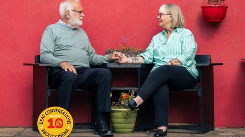 A couple sit at a table holding hands and smiling lovingly at one another
