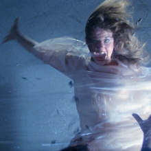 A still from Boorman and the Devil of a woman wrapped in a white sheet in a dramatic pose with her hair blowing in the wind.