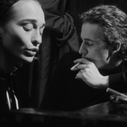 Black-and-white noir portrait of a woman and man sitting together in a dimly lit room, cinematic shadows, cigarette smoke, vintage atmosphere, and dramatic film-style photography.