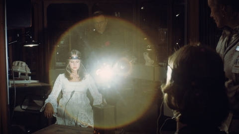 A still from Exorcist II: The Heretic of a girl sitting in a chair with a device on her head with wires coming out of it.
