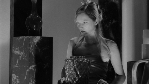 Black and white photo of a woman in a sleeveless dress sitting behind a table with a large textured glass vase.