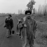 A still from The Jackal of Nahueltoro of two men walking on a rural road, carrying belongings, with leafless trees and overcast skies in the background.
