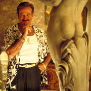 A still from The Birdcage of a man standing next to a statue.
