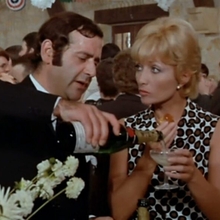 People dressed formally pouring and holding champagne glasses at a lively indoor party with floral decorations.