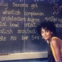 Person in yellow sitting beside a blackboard with handwritten text describing a "Homely Saxena girl" and personal details.