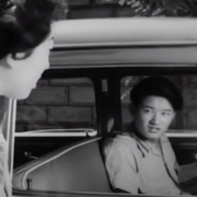A woman looks into a car to have a conversation with the driver.
