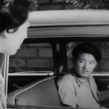 A woman looks into a car to have a conversation with the driver.
