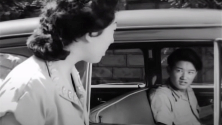 A woman looks into a car to have a conversation with the driver.